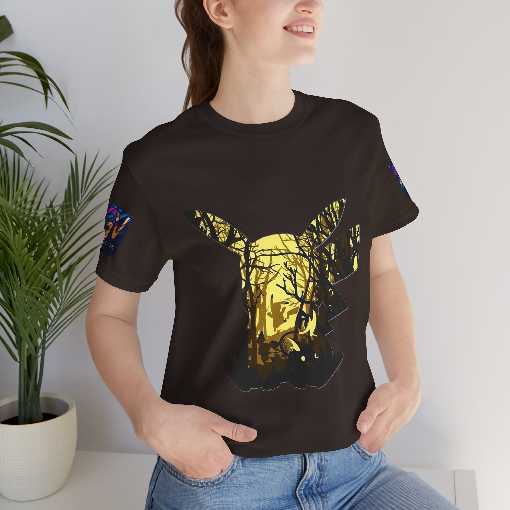 Person wearing a black t-shirt with a colorful graphic design, standing indoors next to a plant.