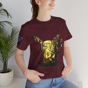 Person wearing a maroon t-shirt with a graphic design of a deer in a forest, standing indoors next to a plant.