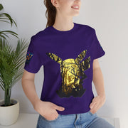Person wearing a purple t-shirt with a gold and black deer design, standing indoors next to a plant.